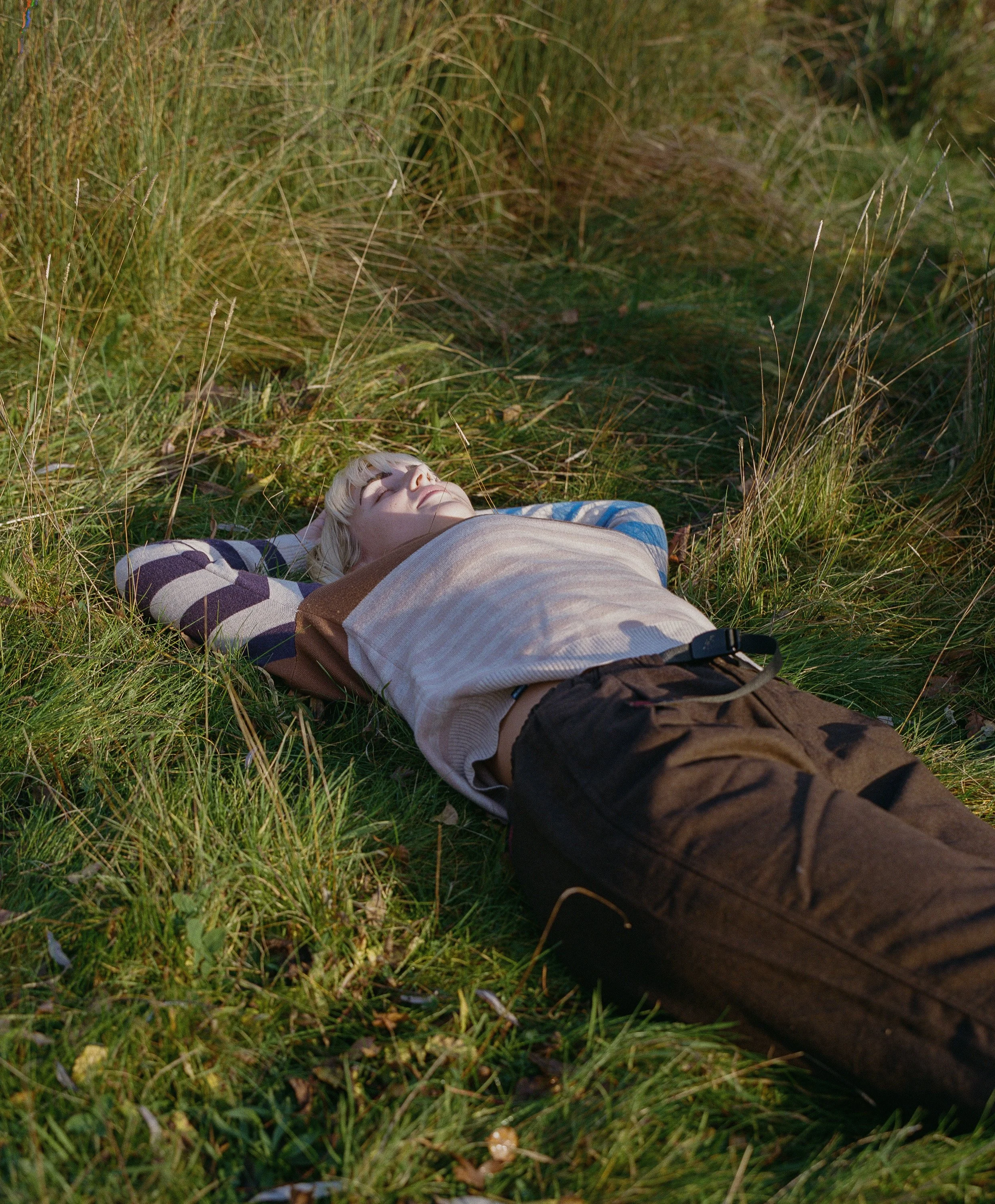 Person lying on grass with eyes closed in a grassy outdoor setting.