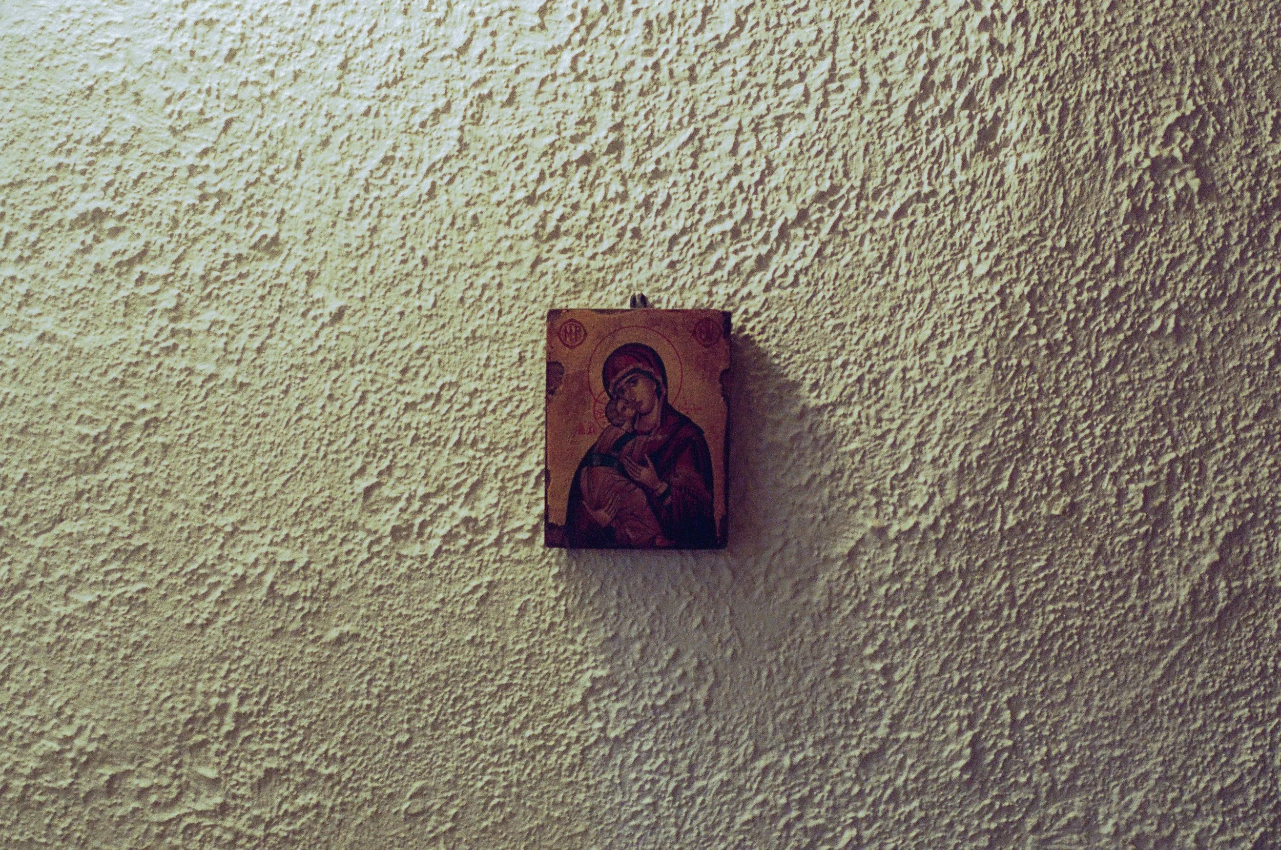 Small religious icon of Virgin Mary holding baby Jesus on a textured beige wall.