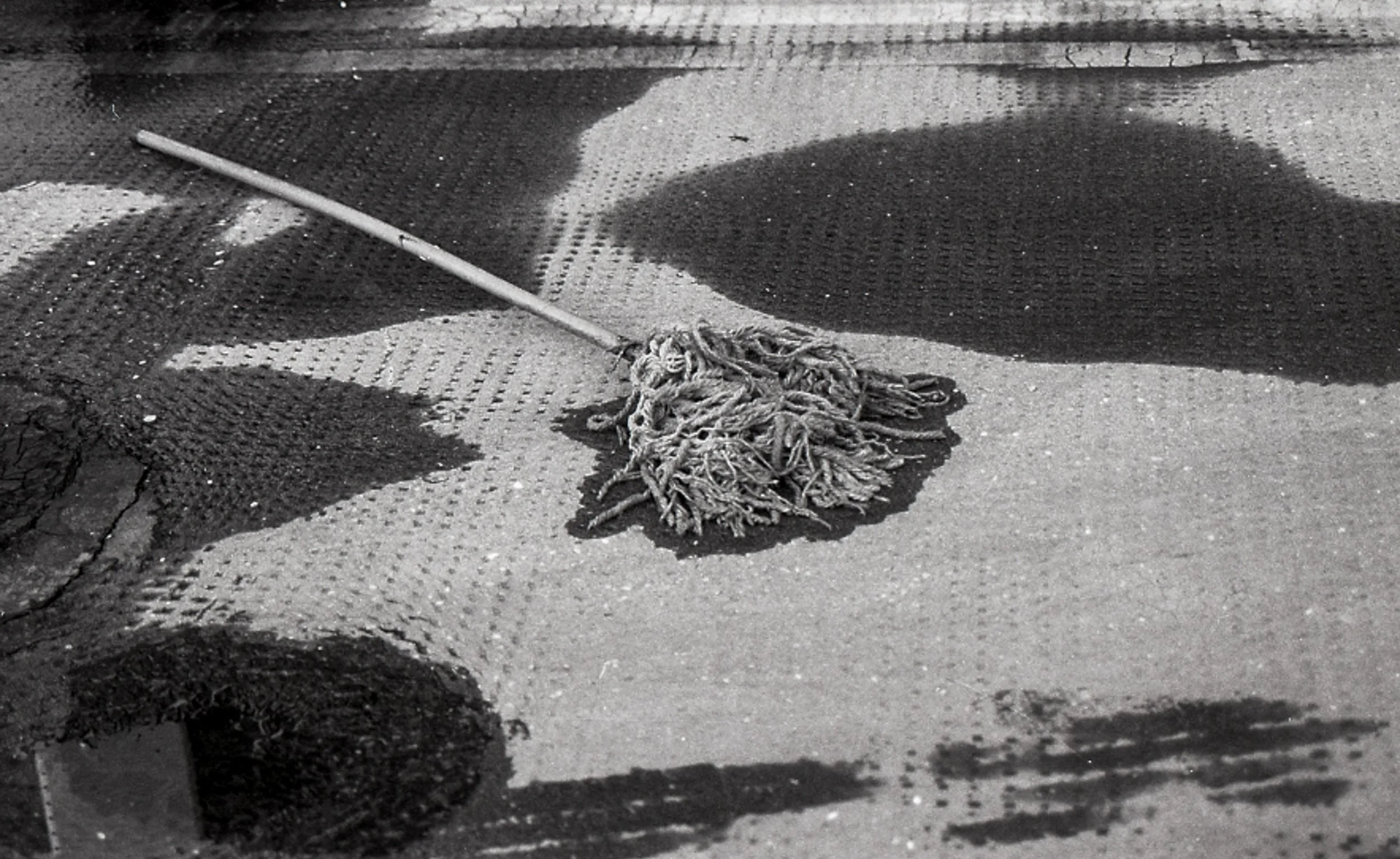 A mop on a concrete floor partially covered with a mesh tarp, with shadows of objects and a person visible.