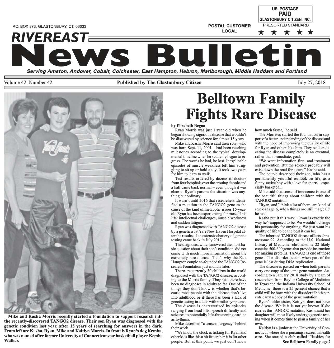 Family portrait with one young boy, a young adult female, a man, and a woman standing in a home interior. The younger boy is holding a large dog on a leash.