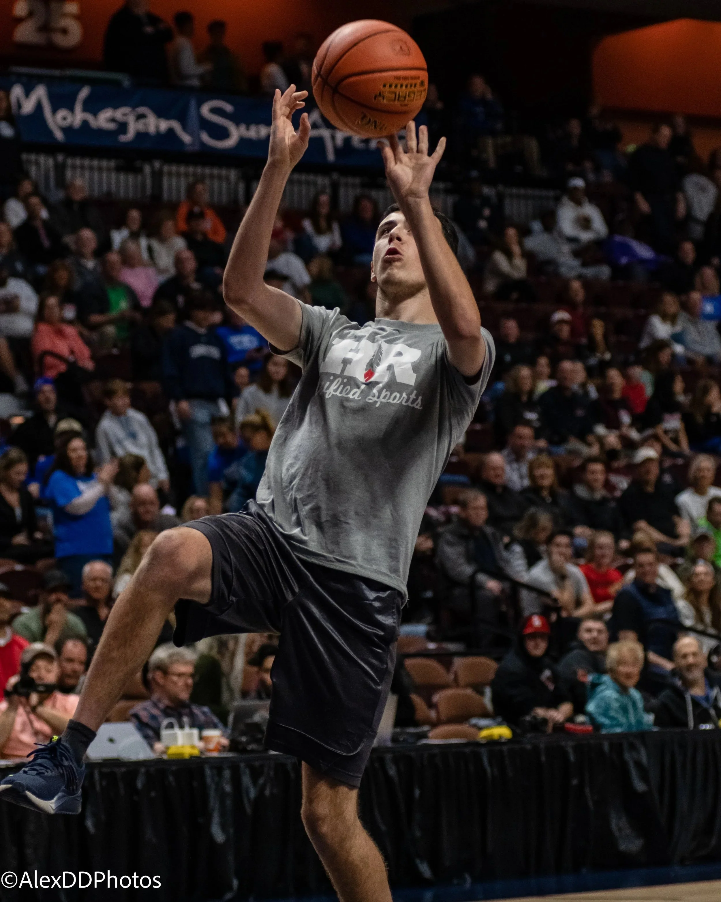 A young man jumping with a basketball in a gymnasium filled with spectators during a game.