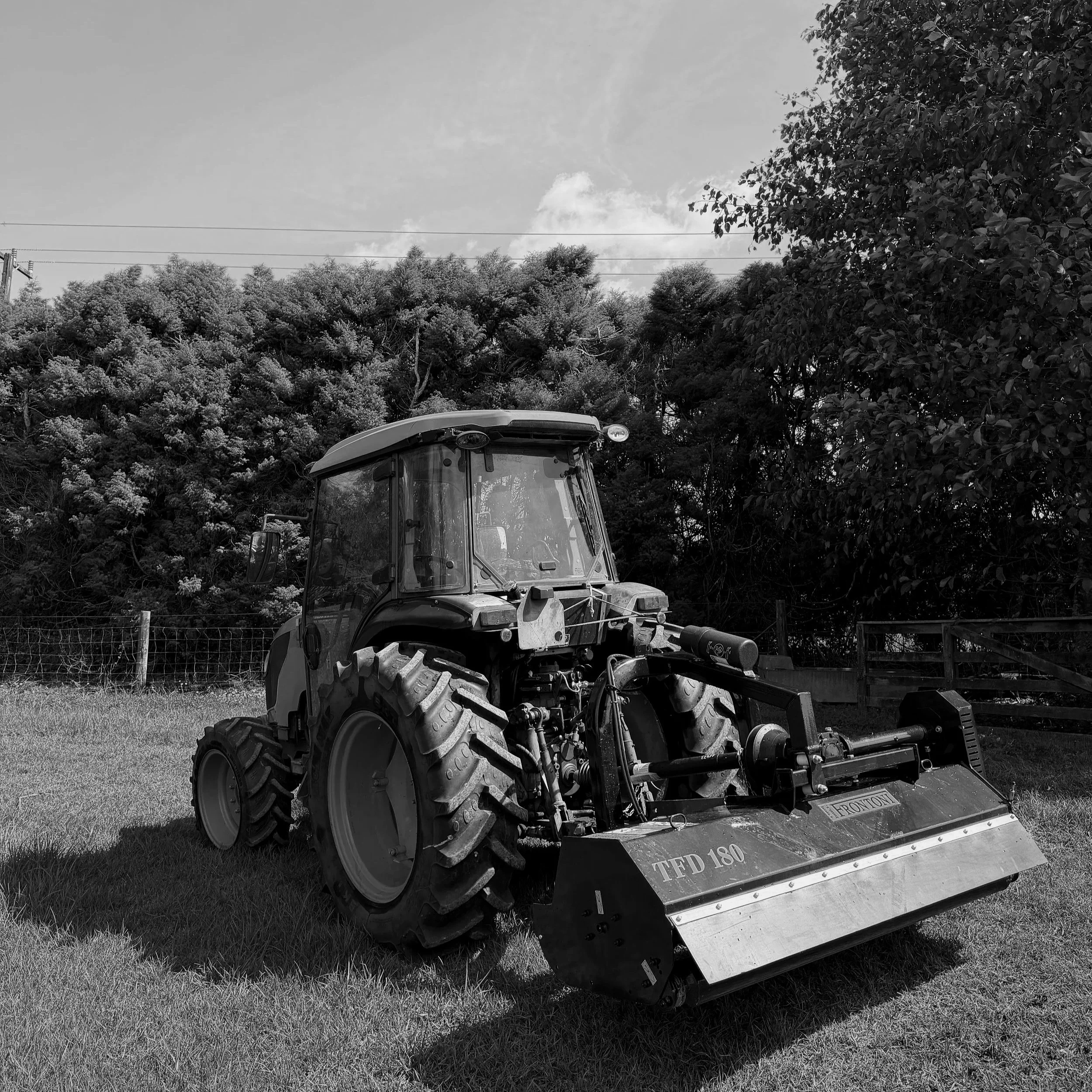 A tractor with a blade attachment in a grassy area with trees and a fence in the background.