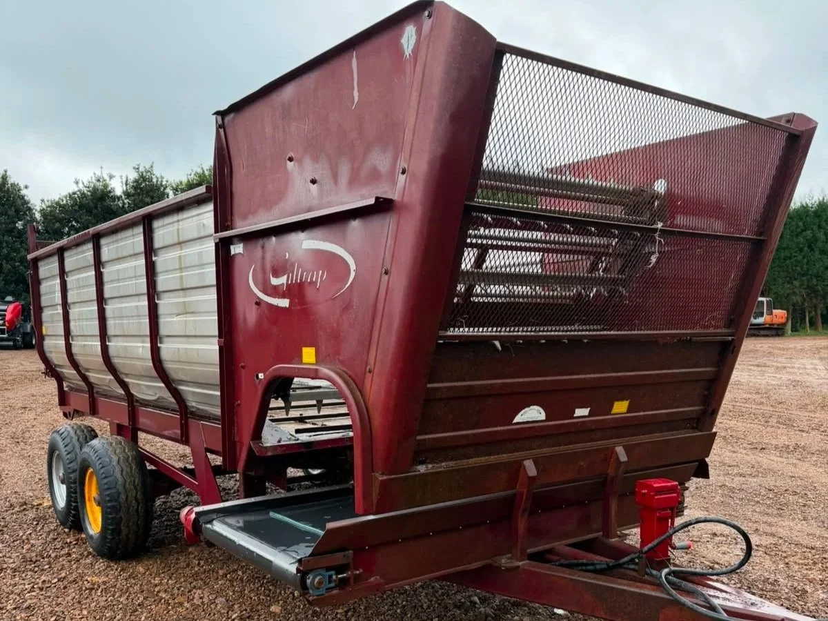 A large red farm wagon with tires, parked on a muddy ground with trees in the background.