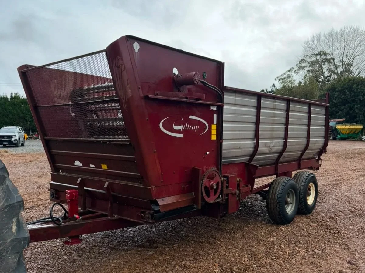 Red farm wagon with metal sides and large tires parked on gravel with overcast sky