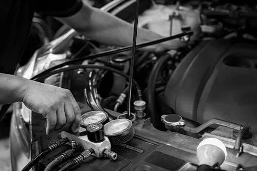 A person working on a car engine, using a tool to measure or adjust a component in the engine bay.