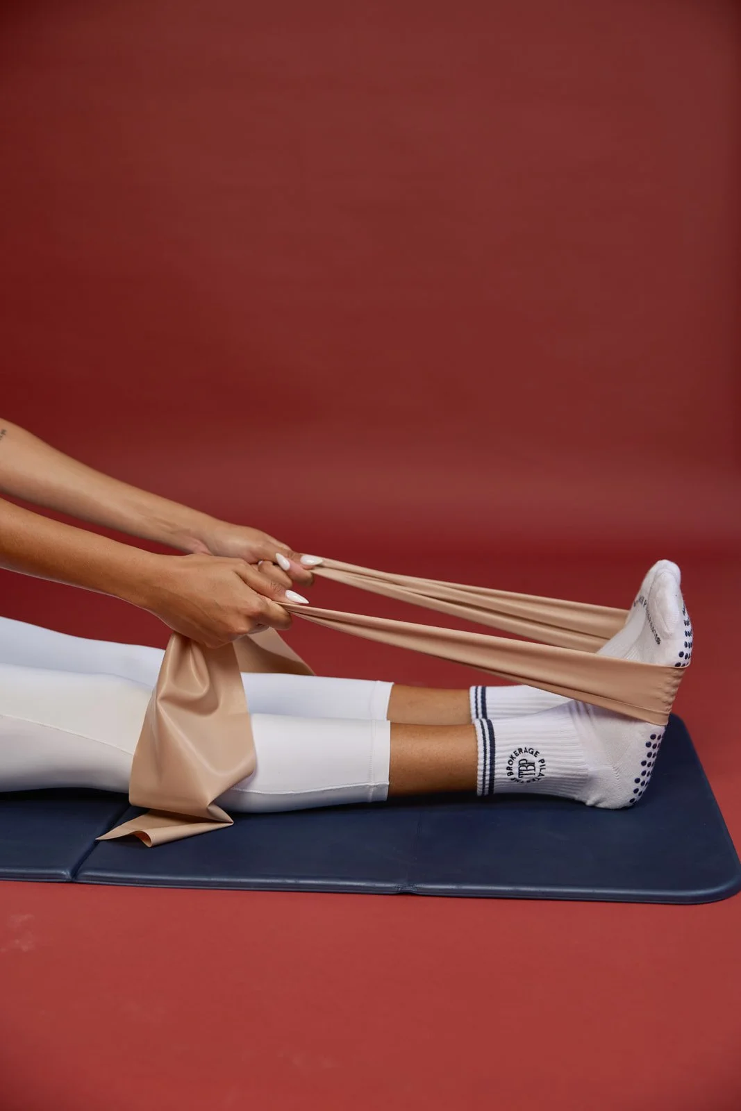 Person stretching their legs using resistance bands while lying on a gym mat against a red background.