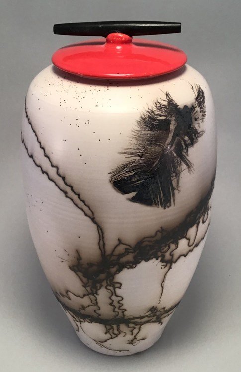 Decorative vase with black ink designs, a red and black lid, and a gray background.