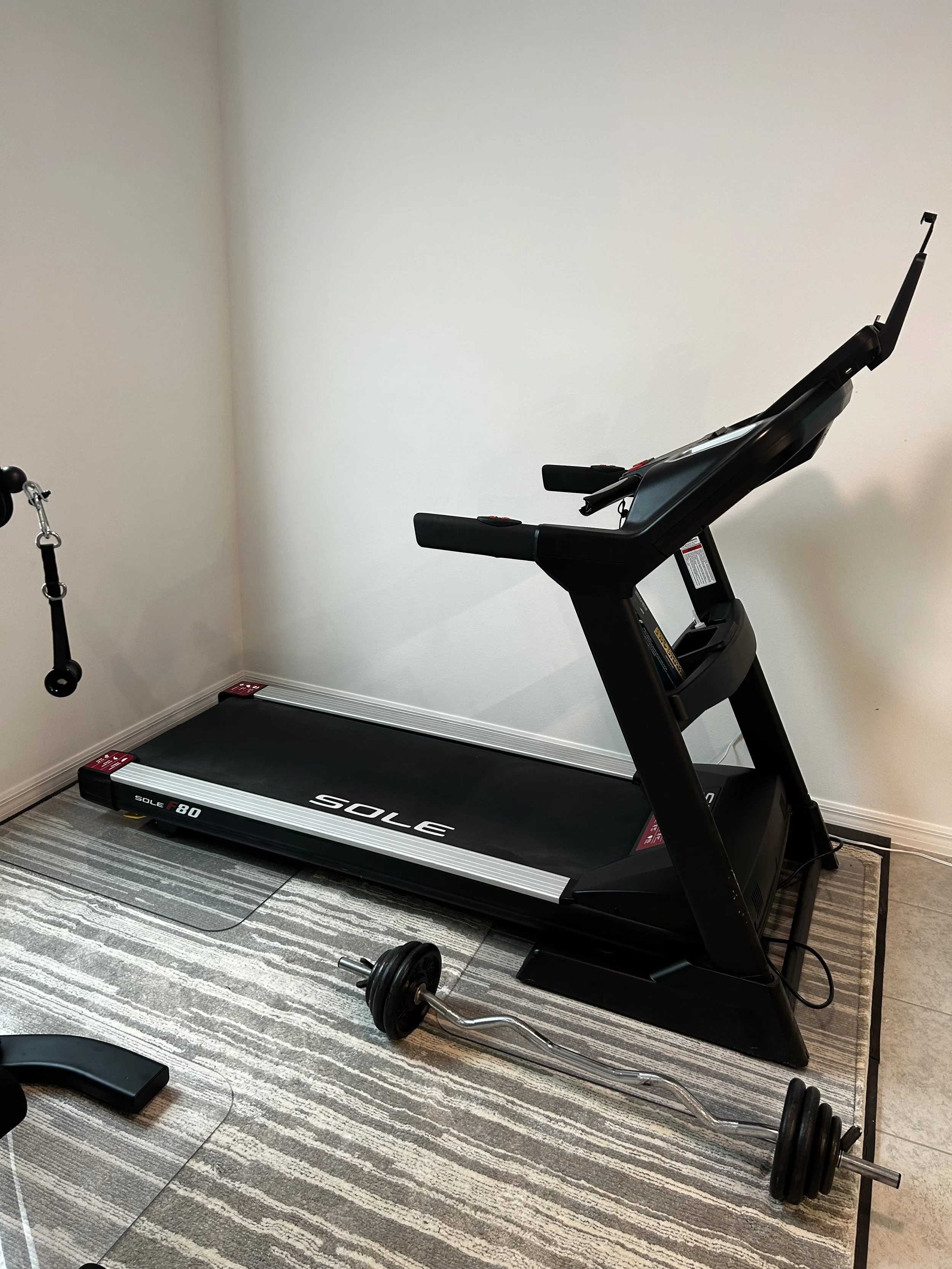A treadmill and a barbell with weights in a home gym corner.