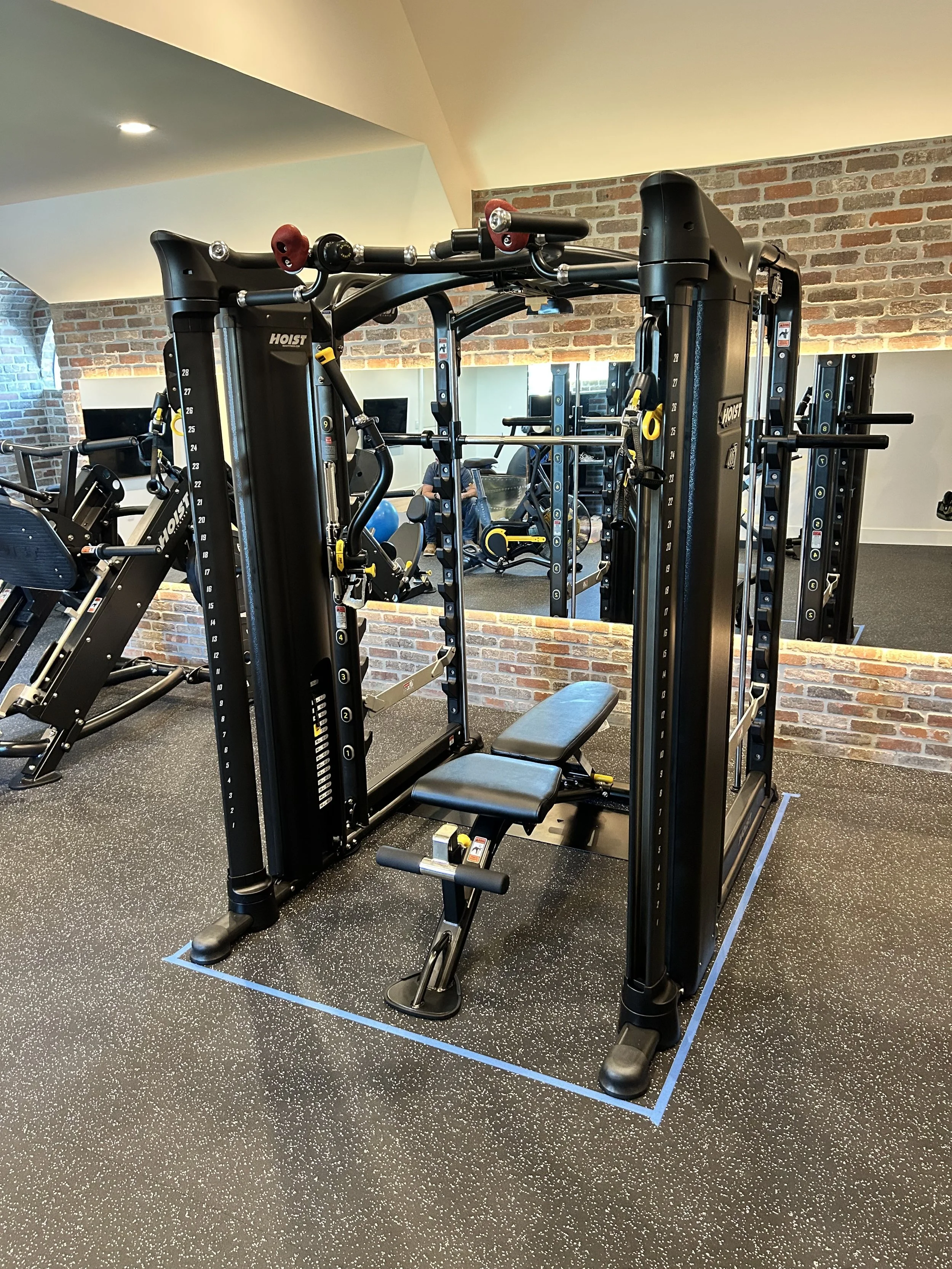 A gym with a black multi-function workout machine and mirror wall in the background