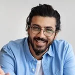 Smiling man with glasses, dark hair, and beard wearing a blue shirt.