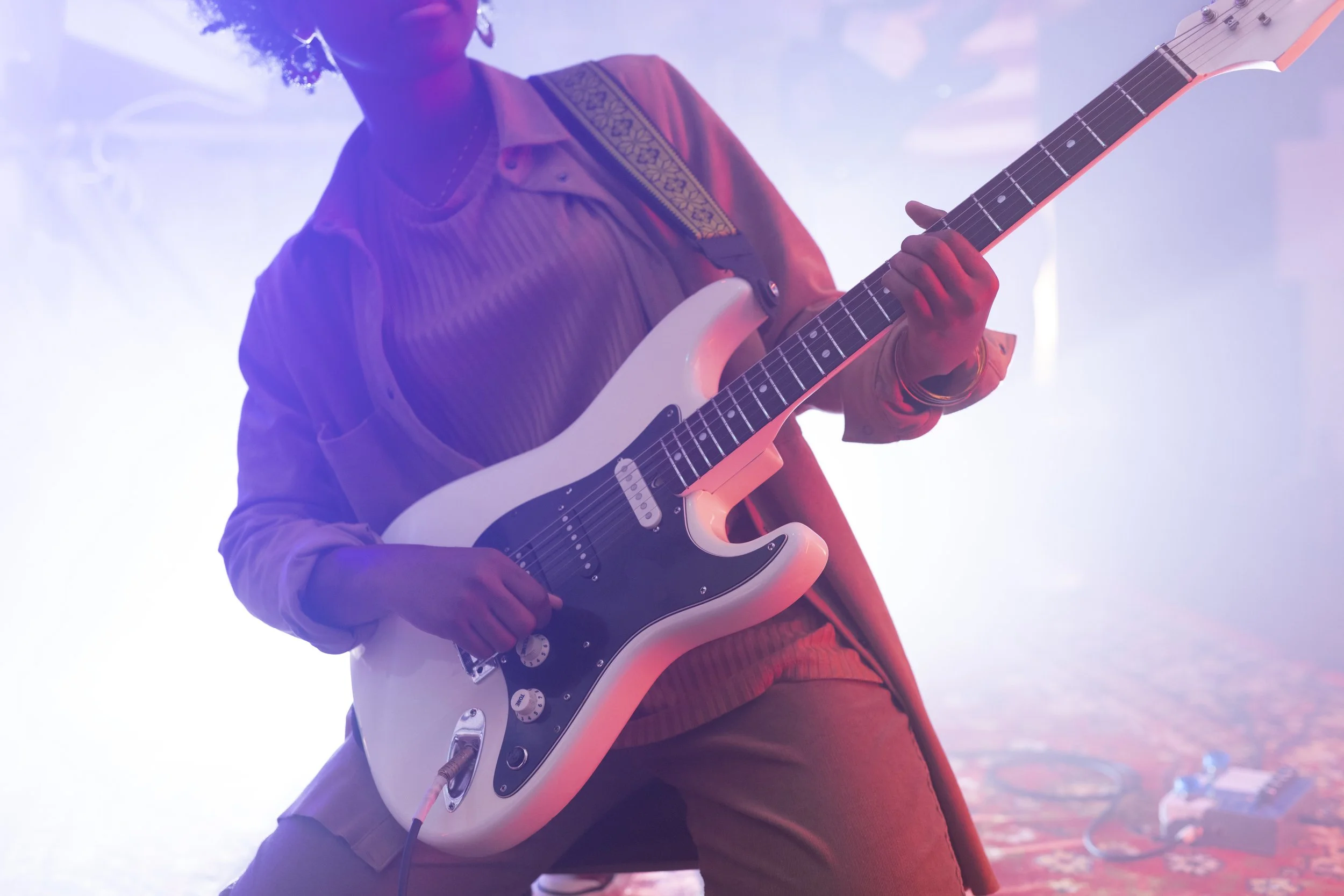 Person playing an electric guitar on stage, illuminated by colorful stage lighting.