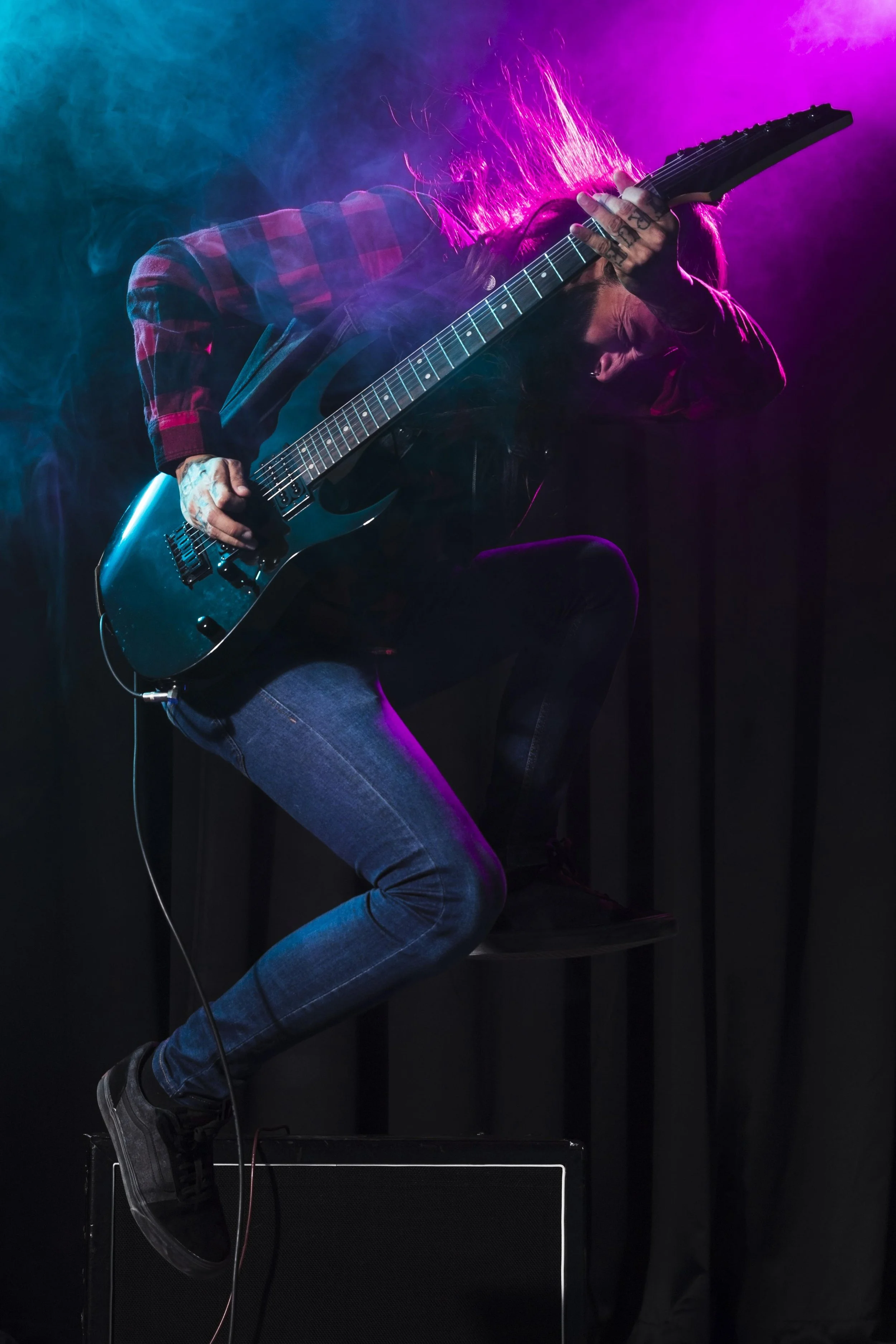 Musician playing an electric guitar on stage with colorful lighting and smoke effects.