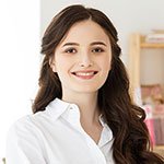 Portrait of a young woman with long, dark hair, smiling and wearing a white shirt, in an indoor setting.
