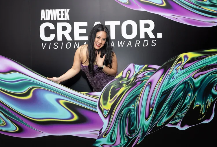 Woman standing in front of a black backdrop with text at the "Adweek Creator Visionary Awards," with colorful, swirling abstract fabric.