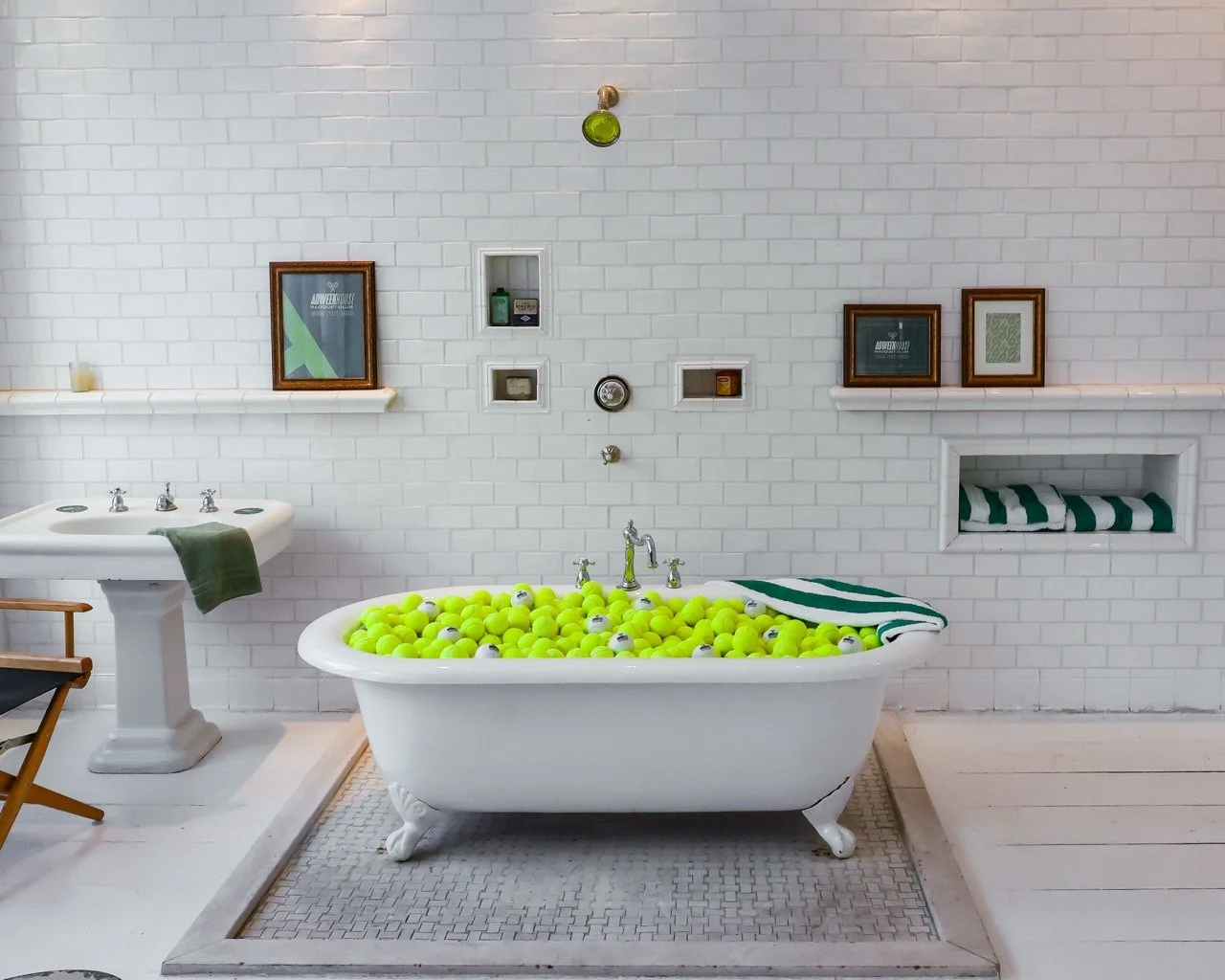 Bathroom with a bathtub filled with yellow tennis balls, a vintage sink, framed pictures on the wall, and a towel on the edge of the tub.