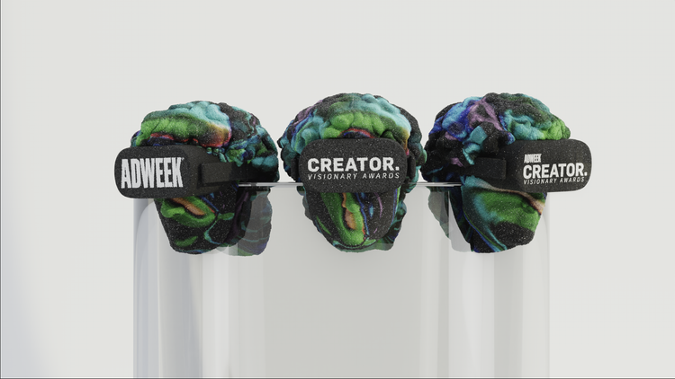 Three colorful brain sculptures with black bands labeled 'Adweek' and 'Creator' on display on clear stands.