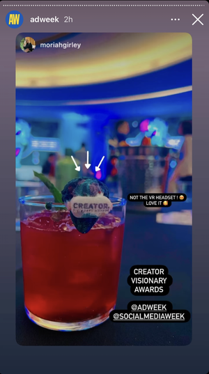 A red cocktail drink with a layered lime wedge, a small edible decoration with the words 'CREATOR' and 'VISIONARY AWARDS' on it, and colorful, blurred background lighting.
