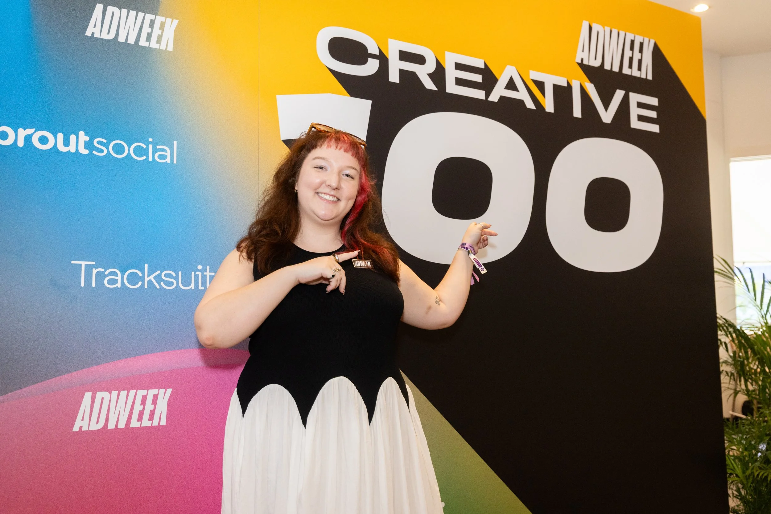 Fiona Kane-Salafia smiling and pointing at a large sign that reads 'CREATIVE 100' at an ADWEEK event.