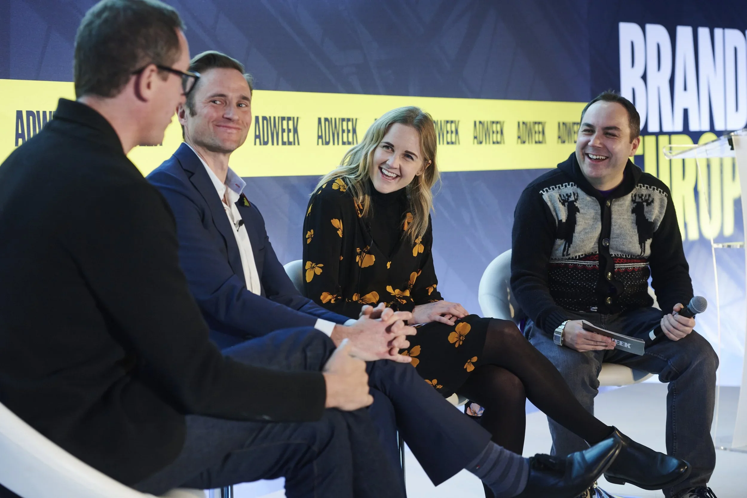 Four people sitting on a panel at a conference with a blue and yellow background that reads 'ADWEEK' and 'BRAND'.