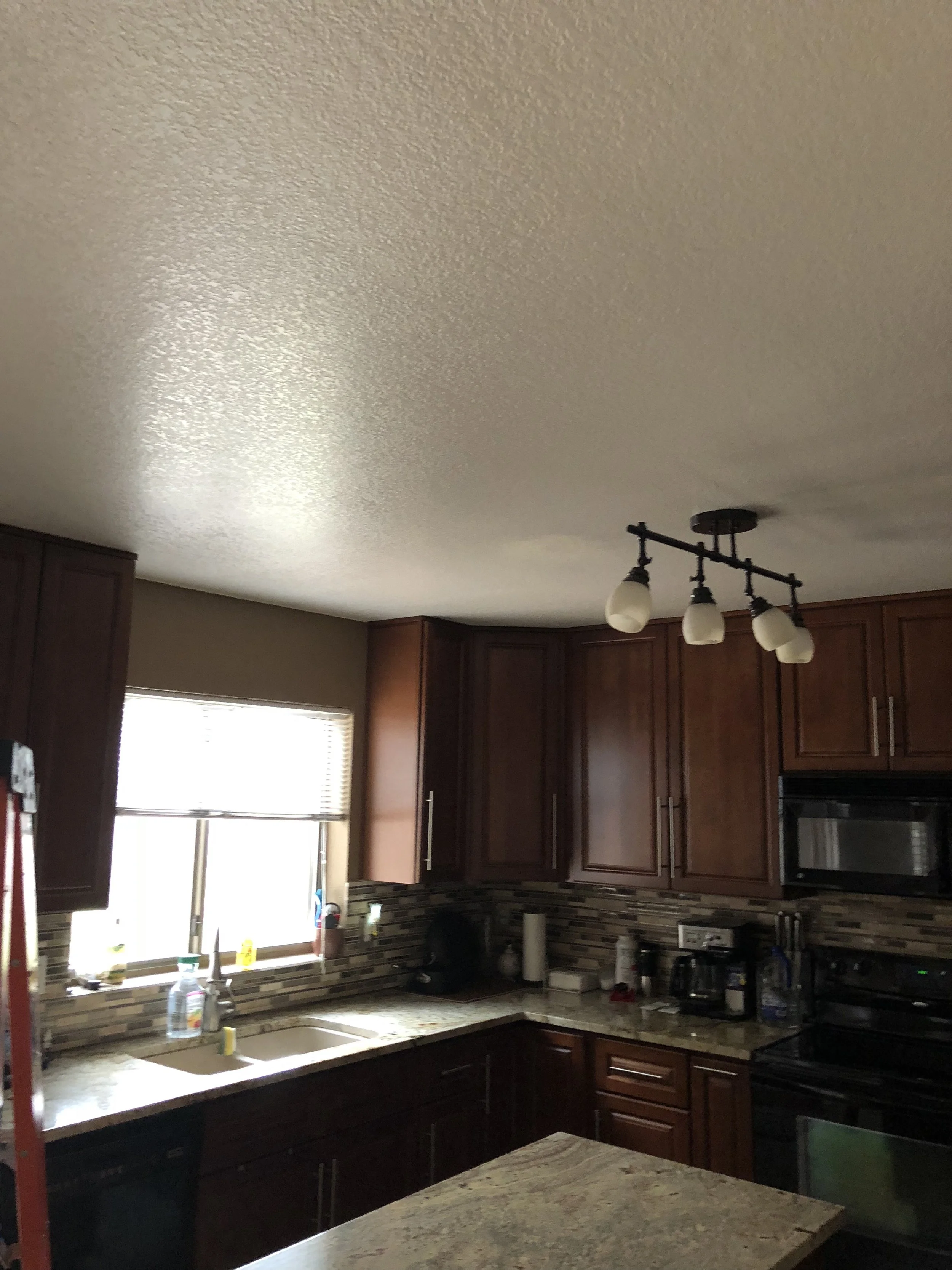 Kitchen with dark wood cabinets, granite countertops, a window with blinds, and a black stove. There is a ceiling light fixture with four bulbs.