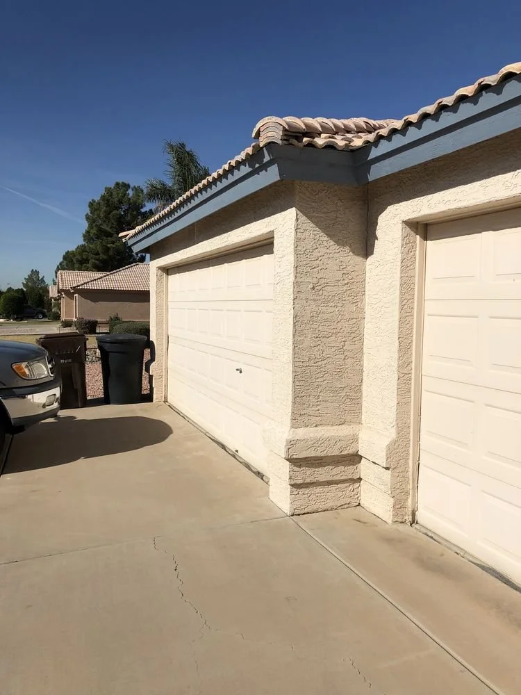 Front view of a house with an attached garage, two trash bins, and a parked car in sunny weather.