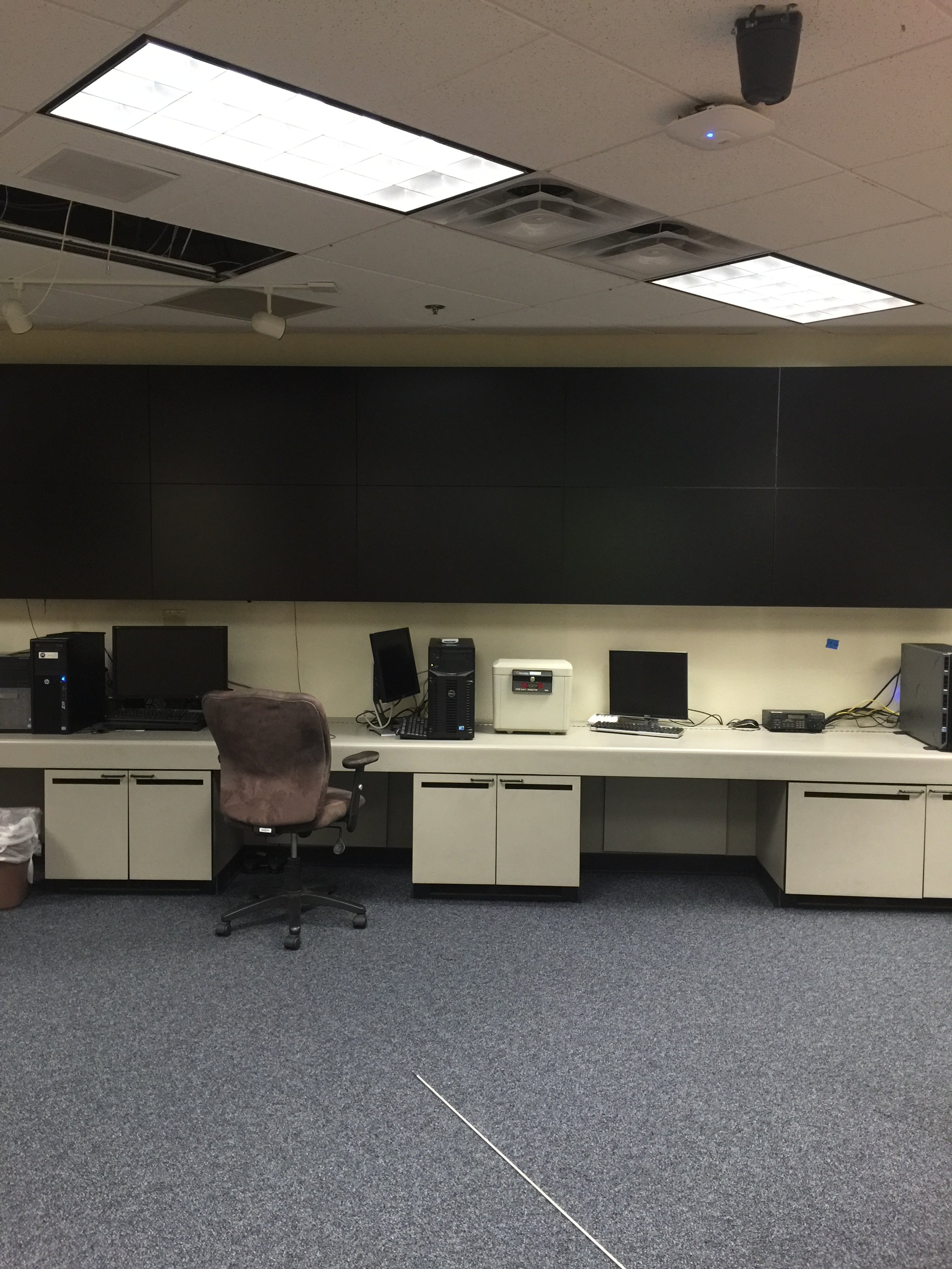 an empty office with a desk, a swivel chair, three old computer monitors, a desktop computer, a printer, and a trash can in the bottom left corner