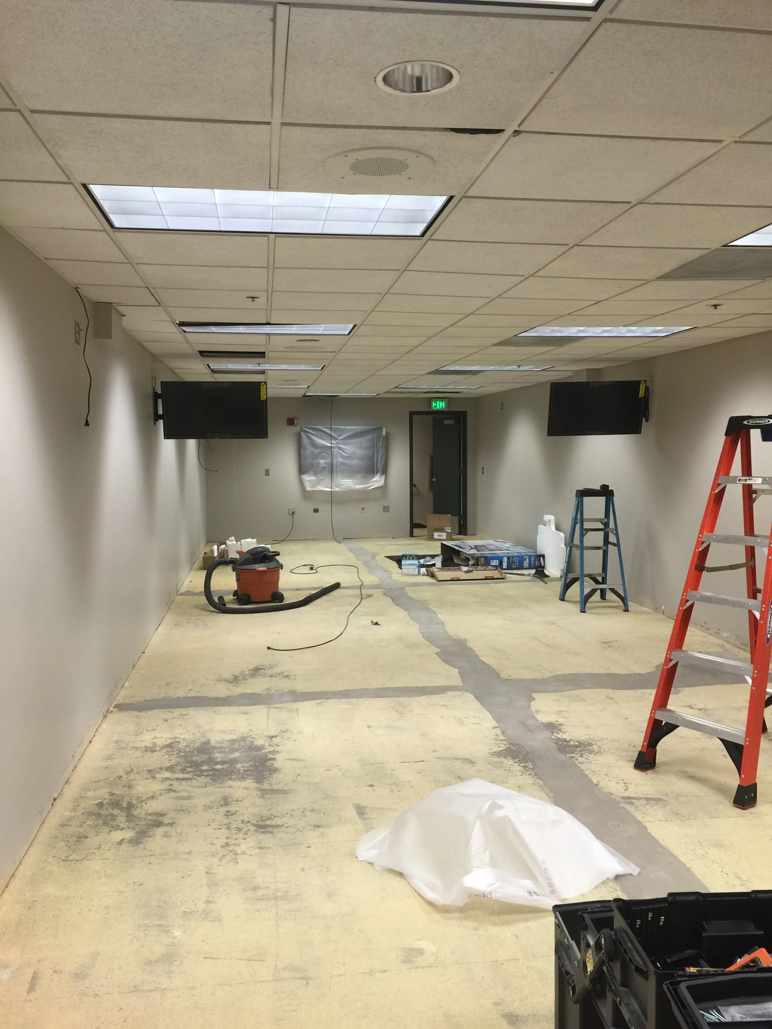 Empty office room under renovation with ladders, tools, and covered equipment.