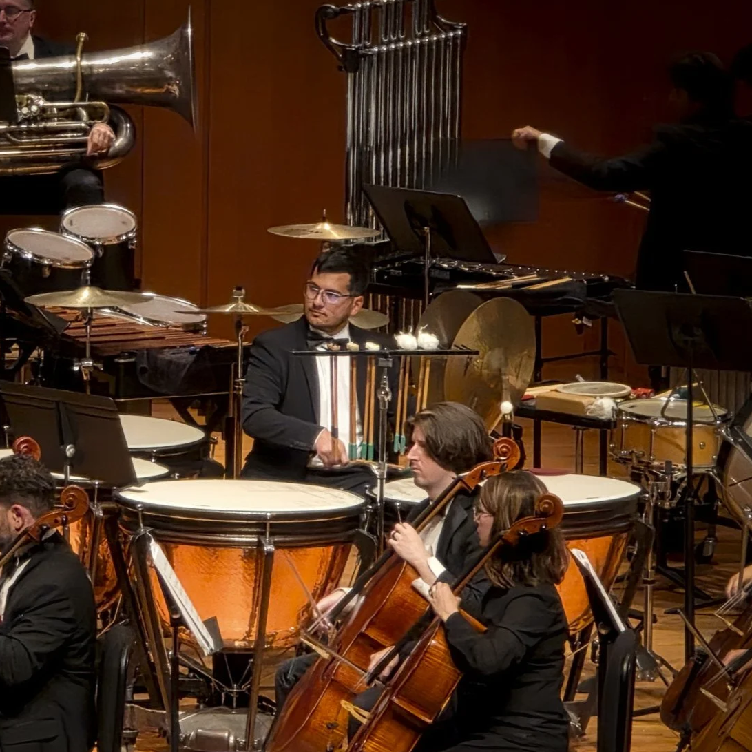 An orchestra performance with musicians playing percussion, violins, and horns on stage.