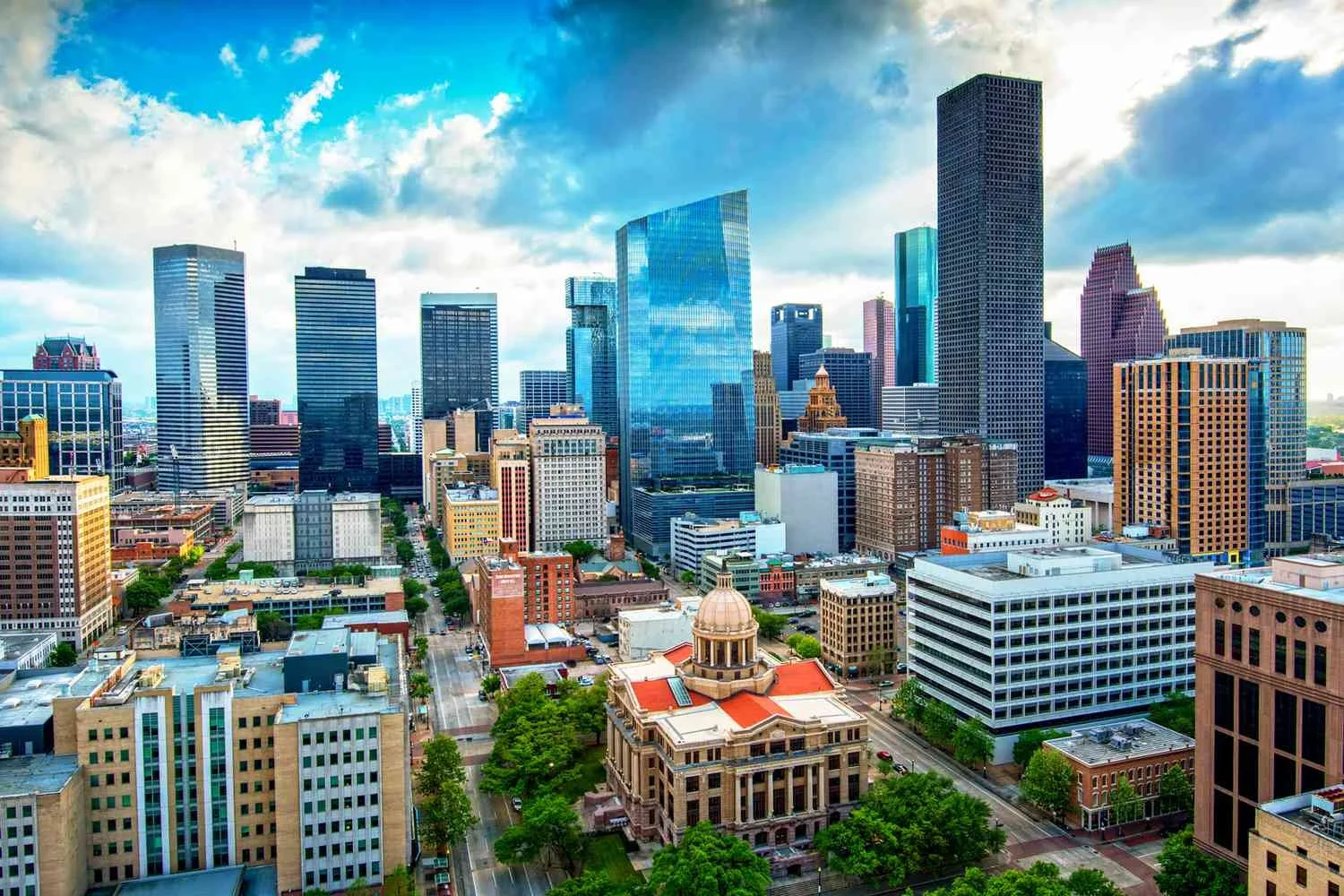 Aerial view of downtown Houston, Texas, with glass skyscrapers, historic buildings, and a cloudy sky.