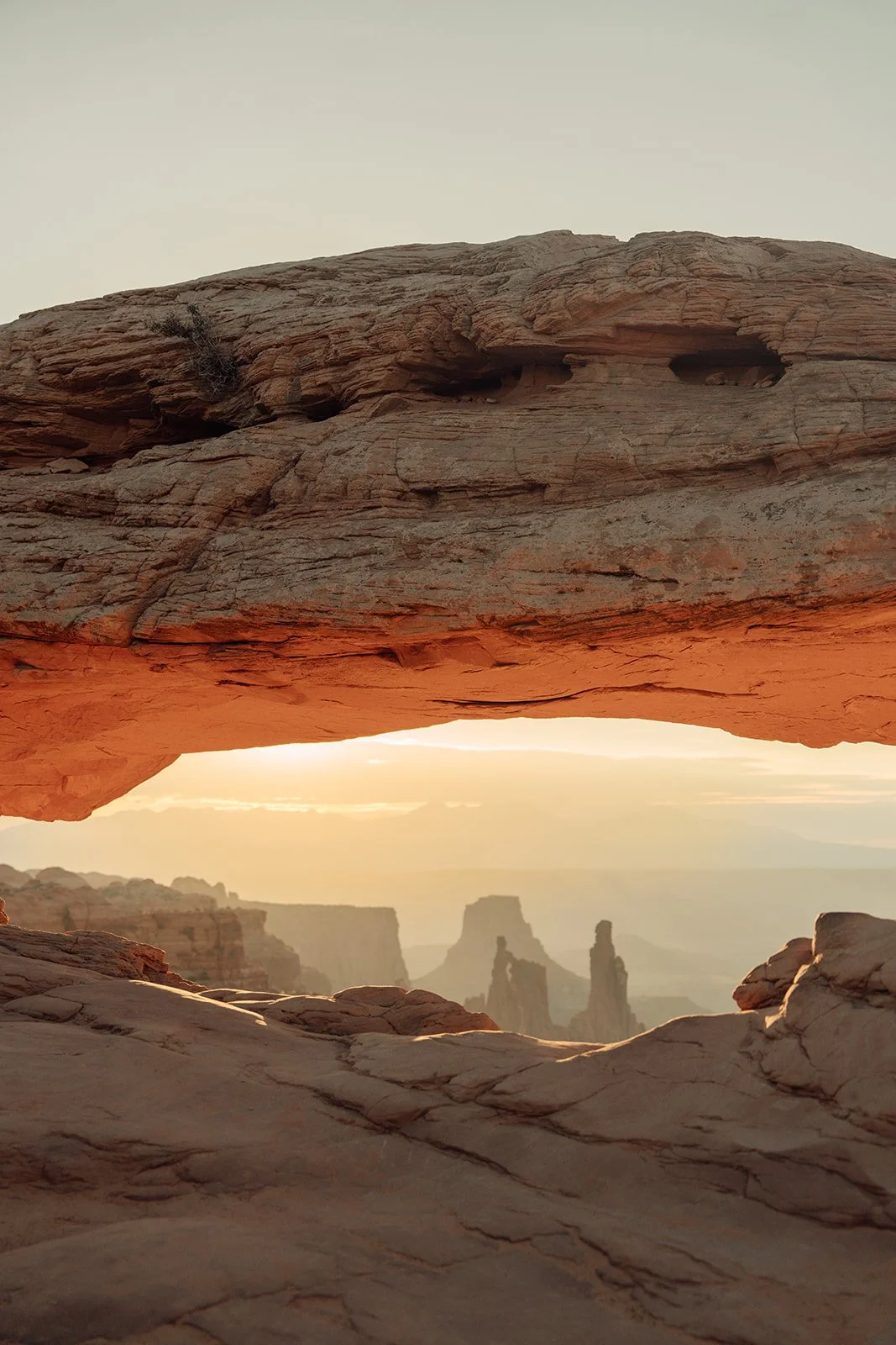 A natural rock arch at sunset with a view of distant rock formations in the background.