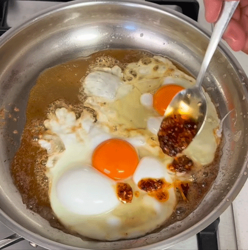 Frying eggs in a pan with soy sauce being added from a spoon.