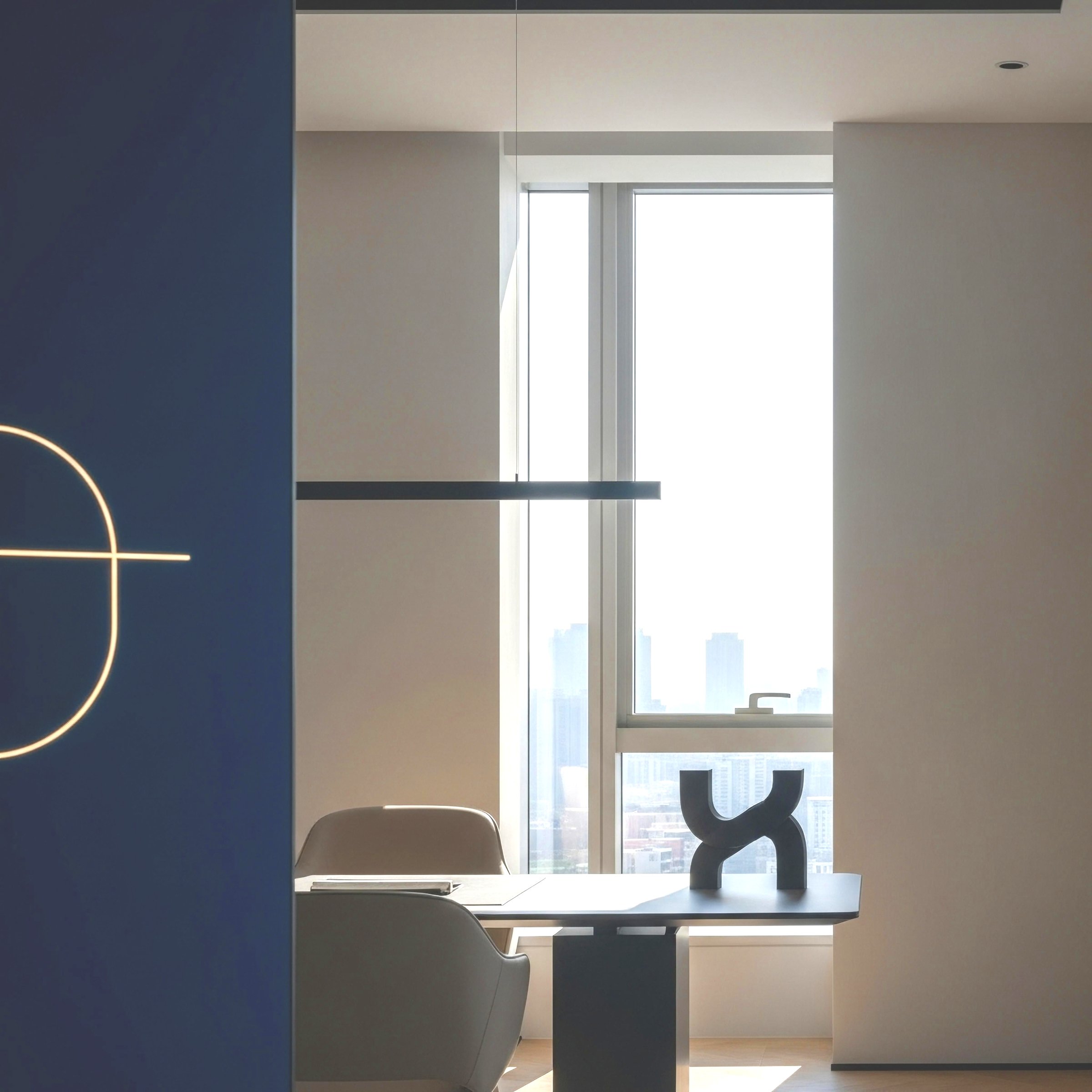 Modern office room with a table, white chairs, a large window with city skyline view, and abstract sculpture on the table.