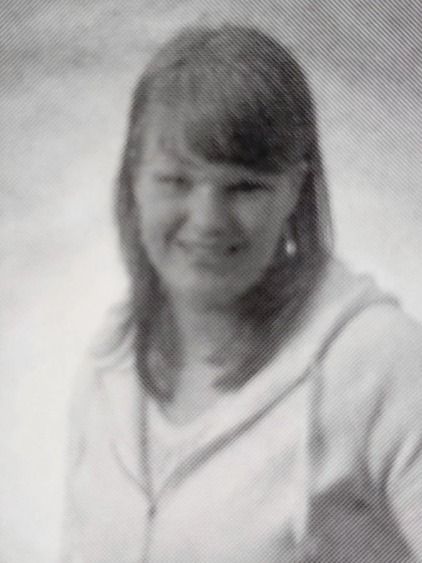 Black and white portrait of a woman with shoulder-length hair, smiling, wearing a light-colored top with dark trim.
