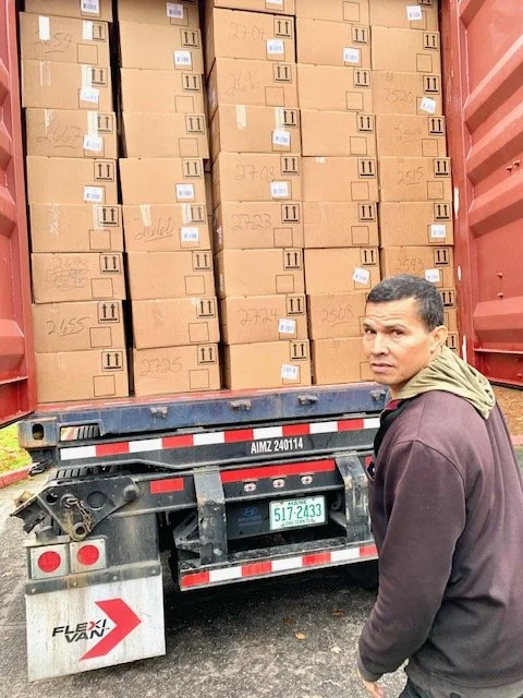 A man standing beside a truck loaded with multiple large cardboard boxes stacked vertically inside the truck.