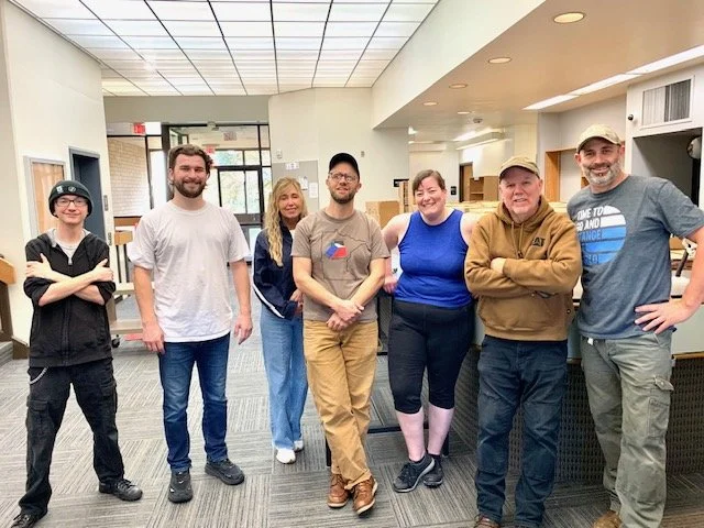 Group of seven people standing inside a modern office lobby, smiling for the photo.