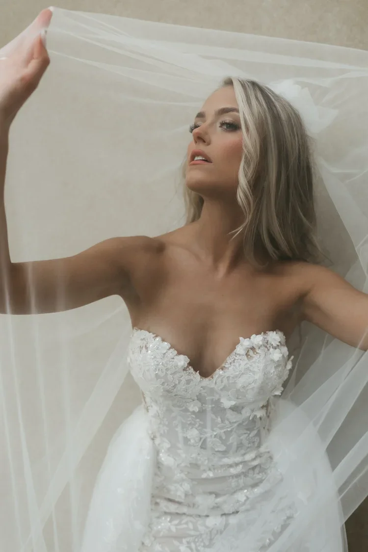 A woman in a wedding dress taking a selfie with a sheer veil.