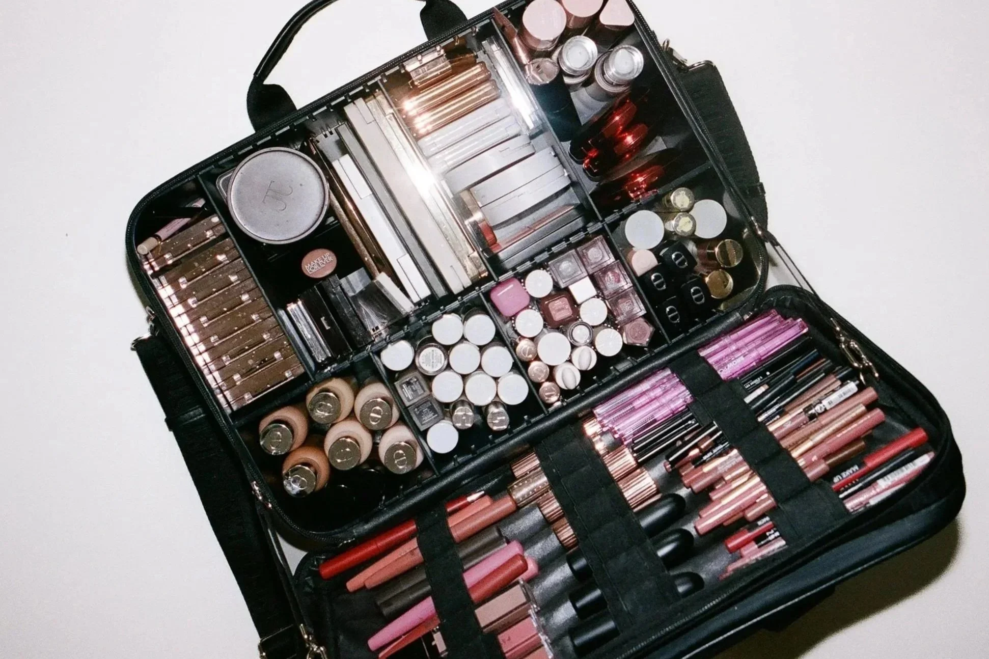 A black makeup bag opened to reveal organized sections filled with various lipsticks, lip glosses, lip liners, and makeup brushes.