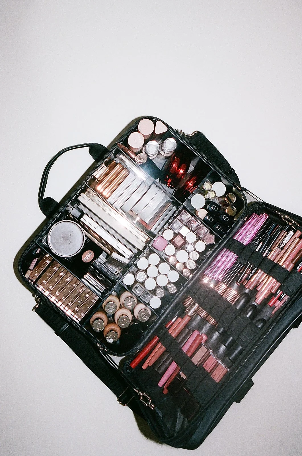 Open makeup kit with lipsticks, eyeshadows, and brushes on a white surface.