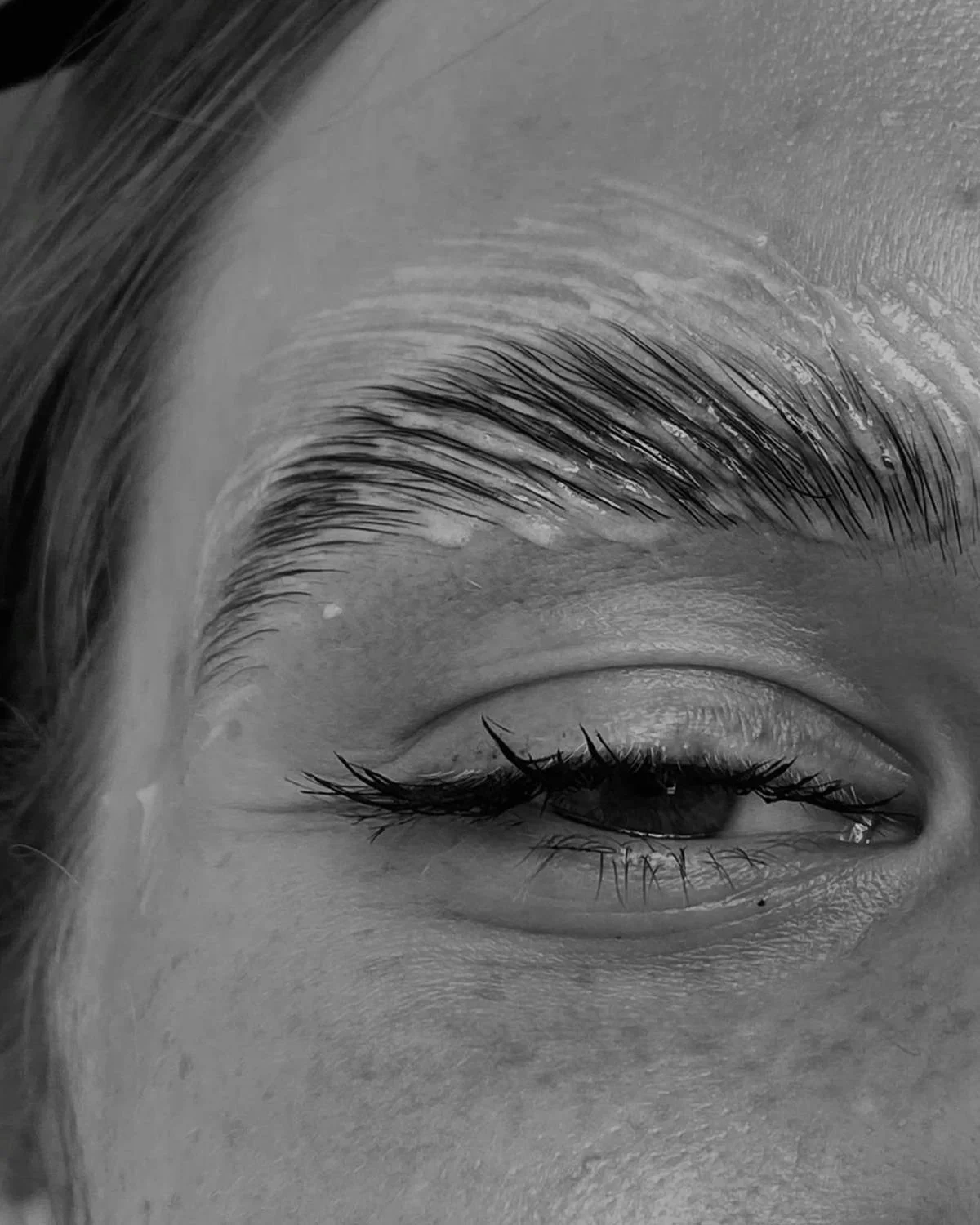 Close-up of a woman's eye with one eyelid partly closed, showing detailed eyelashes and eyebrow.