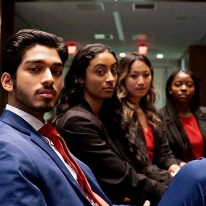 Four young professionals sitting in a conference room, dressed in business attire, looking serious and attentive.