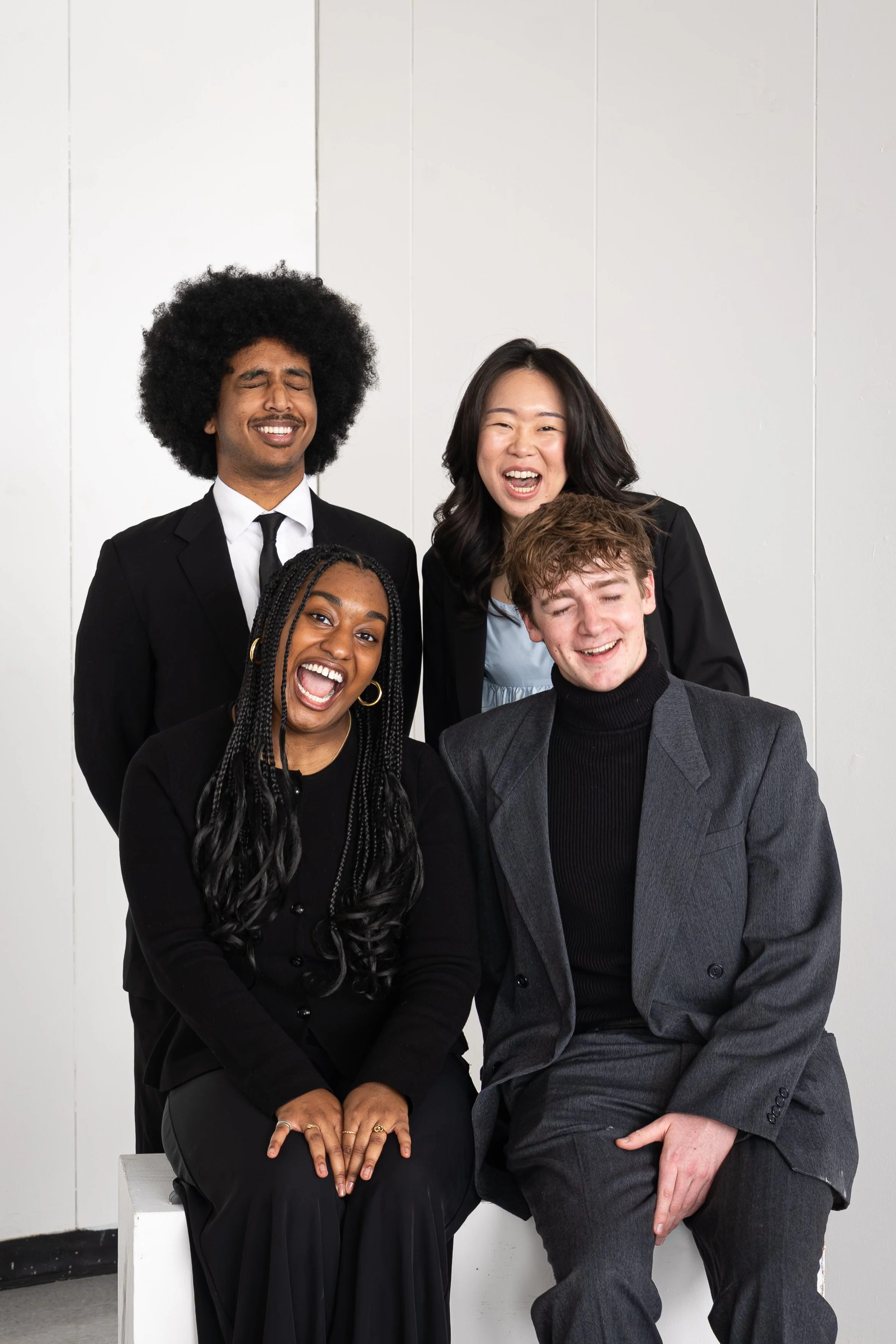 Group of five diverse people in business attire laughing and smiling together in a professional setting.