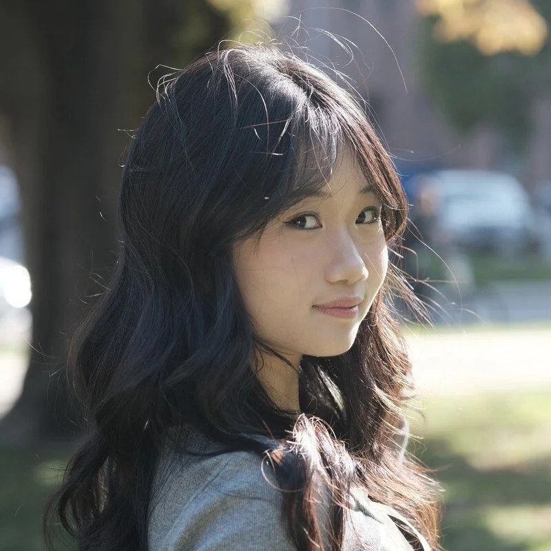 Young woman with wavy black hair smiling outdoors on a sunny day.