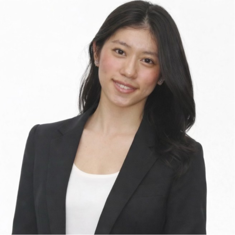 Professional portrait of a young Asian woman with long black hair, wearing a black blazer and white top, smiling against a plain white background.