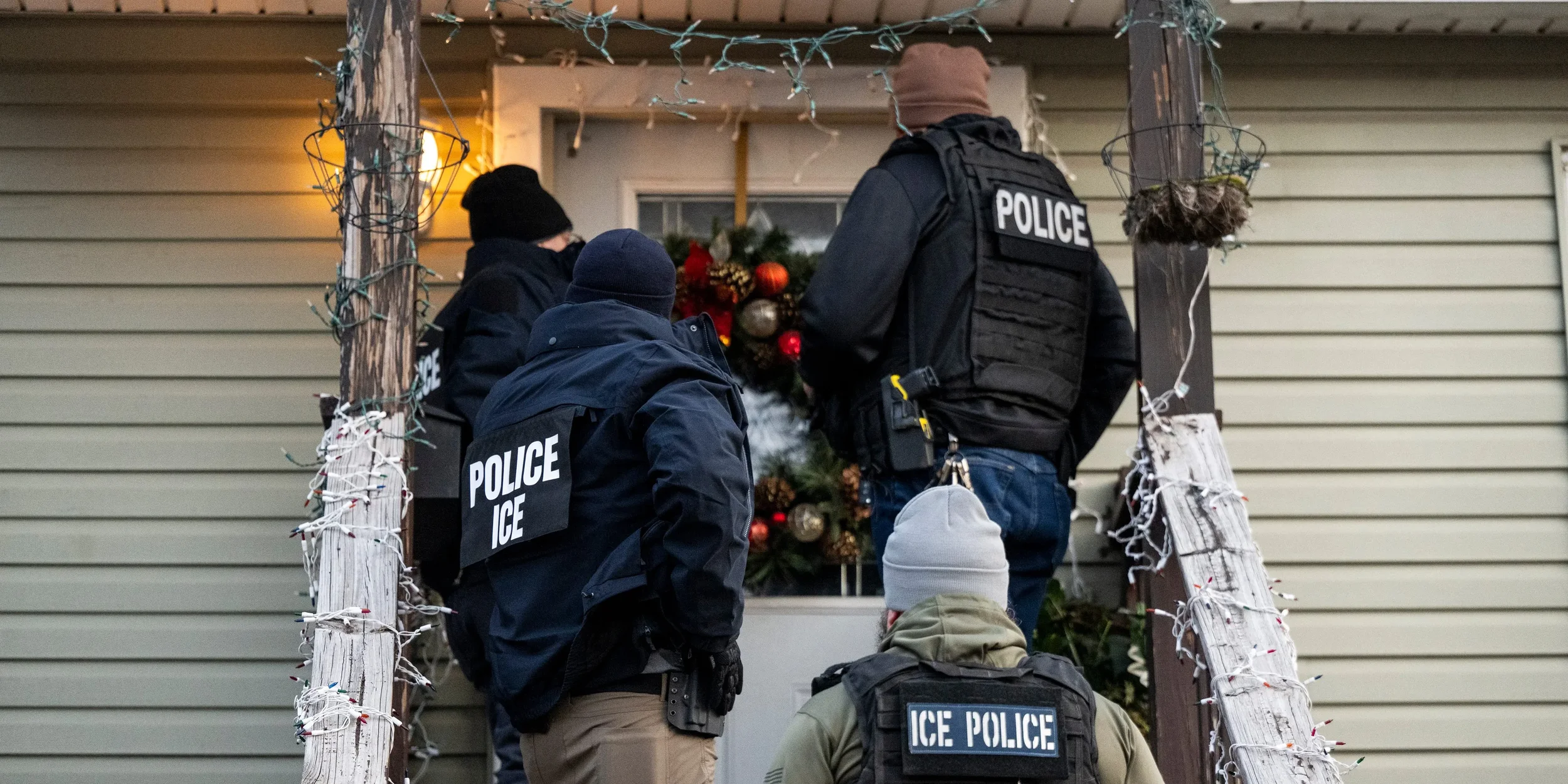Police officers and ice police personnel standing on a porch decorated with Christmas ornaments, near a wreath and holiday lights, during winter.