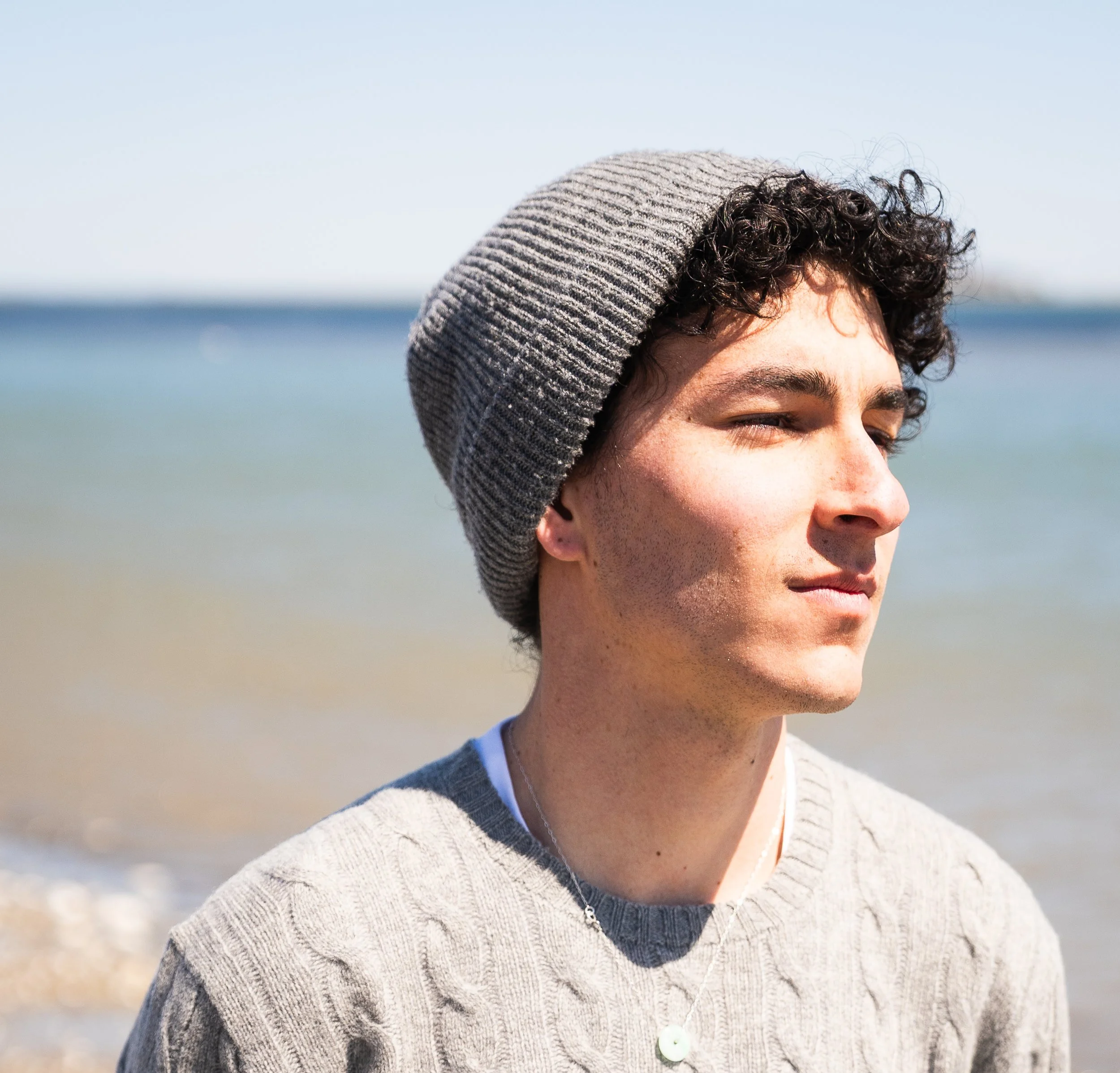 Close-up of a person's face wearing a gray beanie cap and a gray sweater, with a blurred outdoor background.