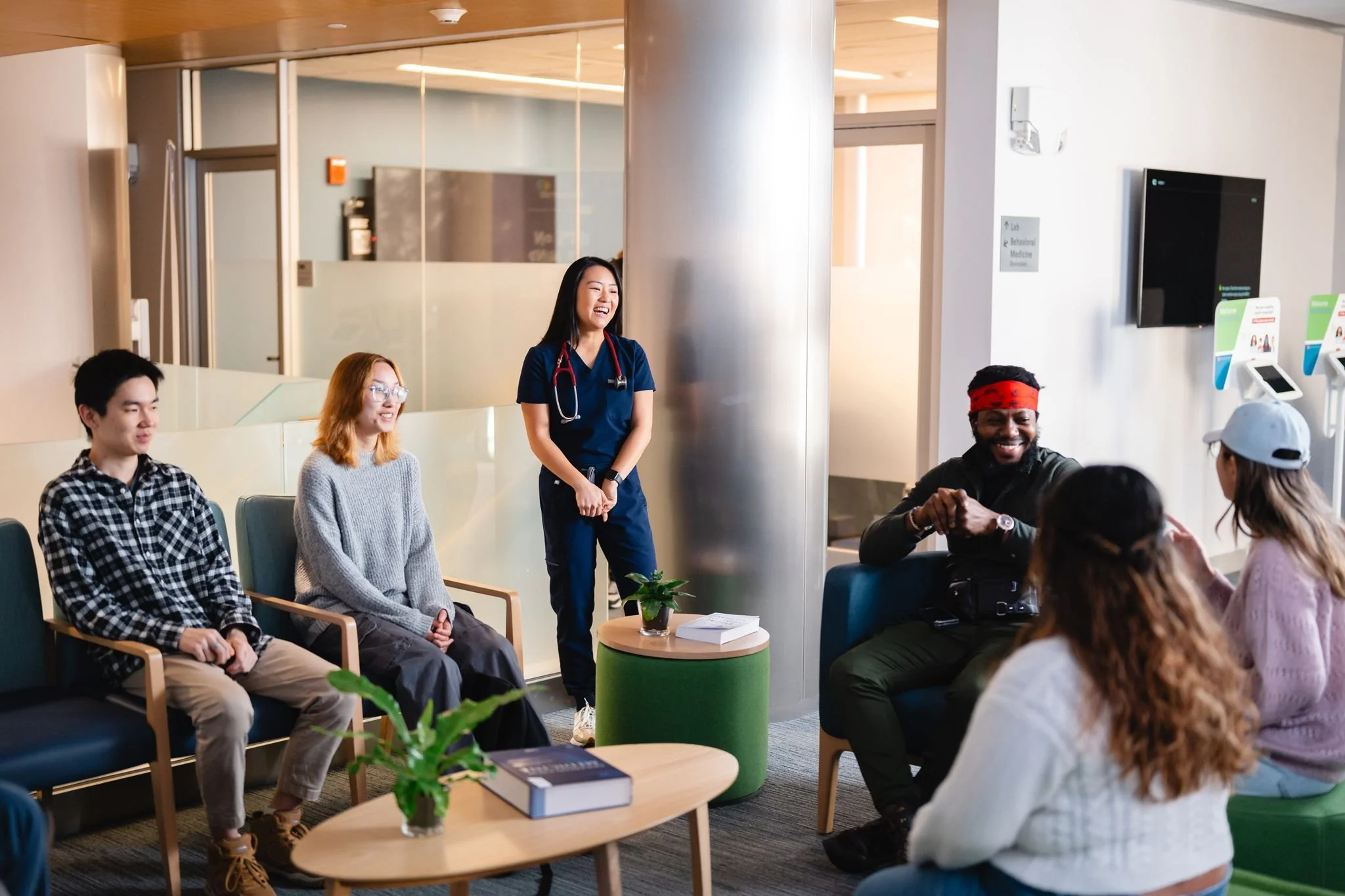 Group of diverse people sitting and standing in a waiting area, smiling and engaging in conversation at a medical facility.