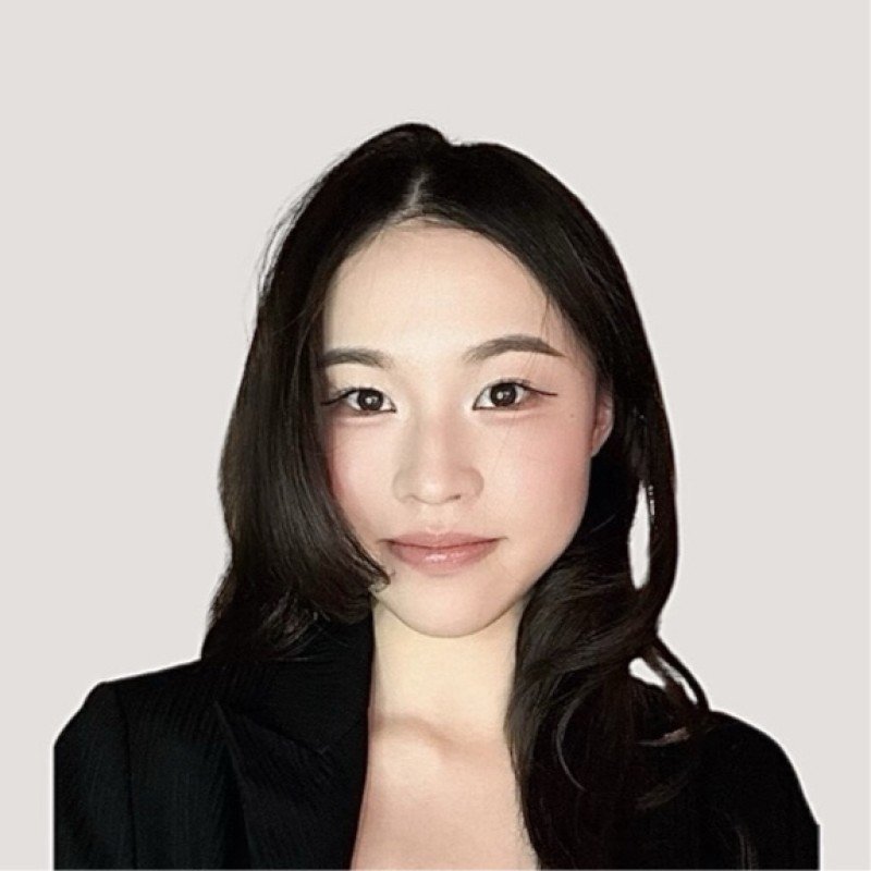 Portrait of a young woman with medium-length black hair, wearing a black blazer, looking directly at the camera with a slight smile, against a plain light background.