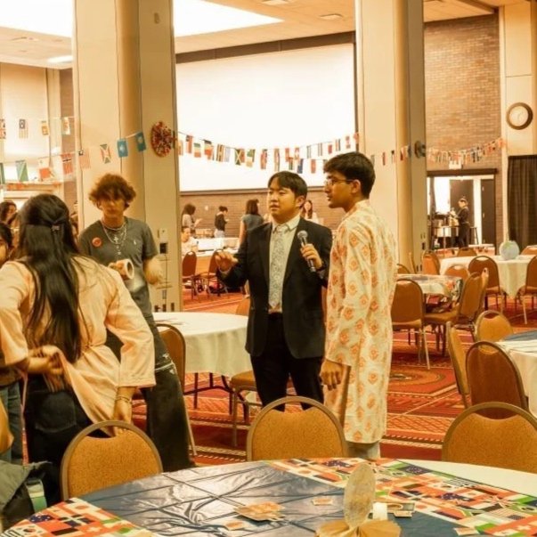 People folding flyers or pamphlets with orange and blue text on a red table, with rolls of stickers nearby, in an indoor setting.