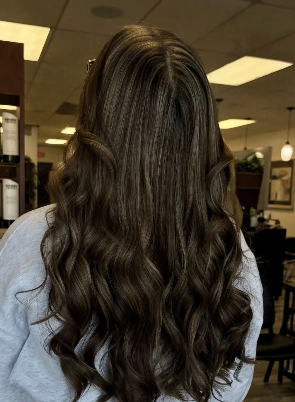 Woman with long, wavy brown hair in an indoor space resembling a salon or cafe.