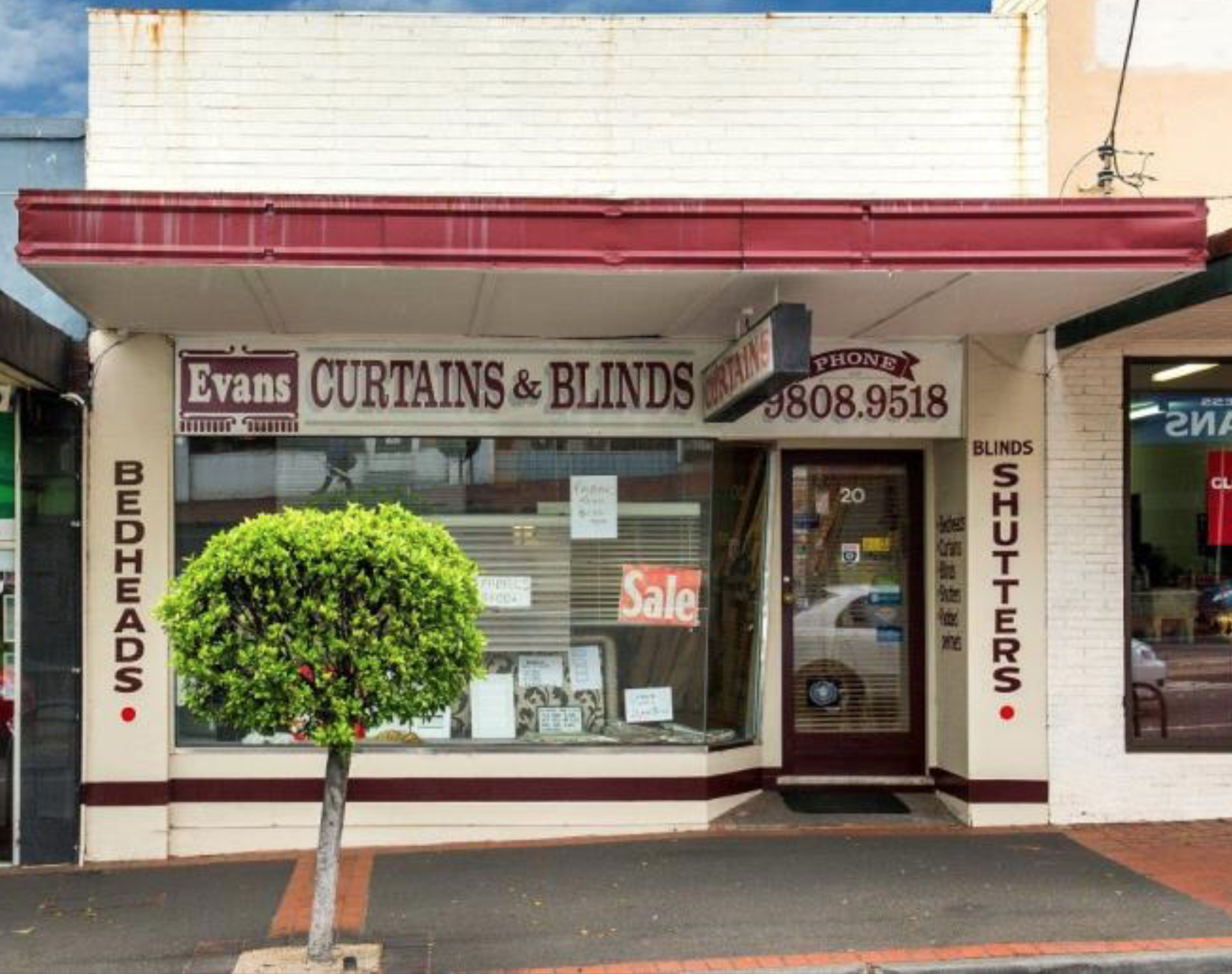 Storefront of Evans Curtains & Blinds with a display window, small tree in front, and signage for curtains, blinds, and shutters.